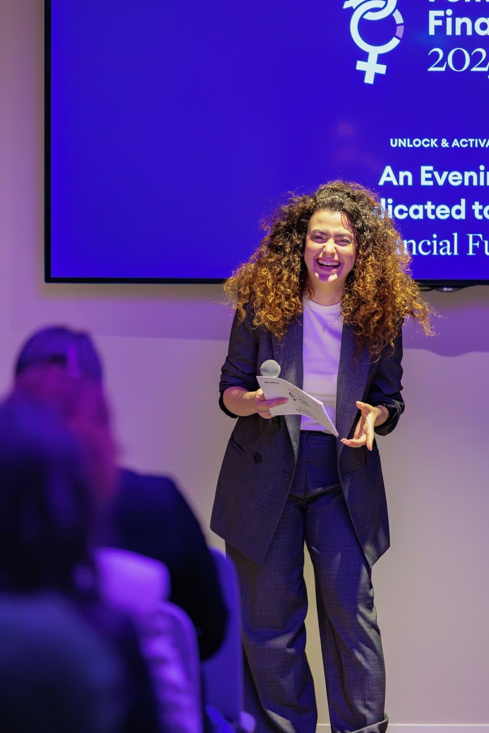 Noam on stage at the Women in Finance 2025 evening, microphone in hand, laughing